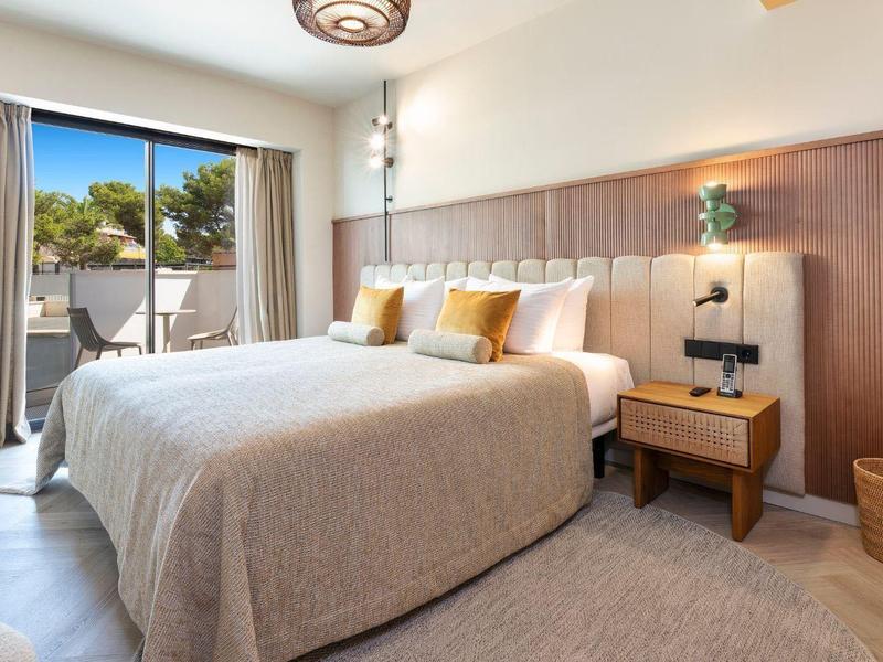 Habitación de hotel moderna con cama doble, muebles de madera y terraza con vista a palmeras.