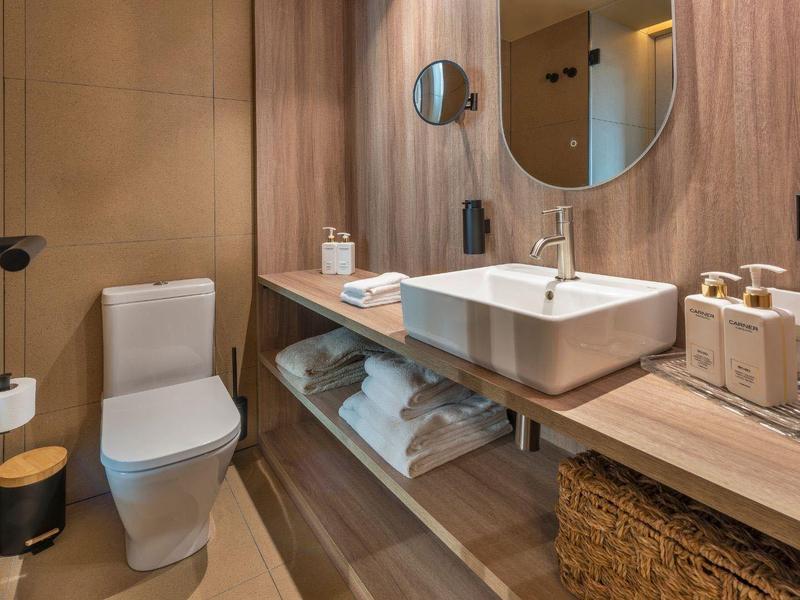 Baño moderno con revestimiento de madera, inodoro, gran espejo y lavabo sobre encimera de madera.