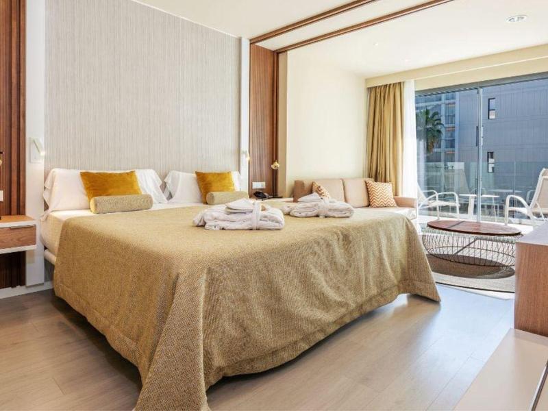 Habitación de hotel moderna con cama king, área de estar y terraza con vista exterior.