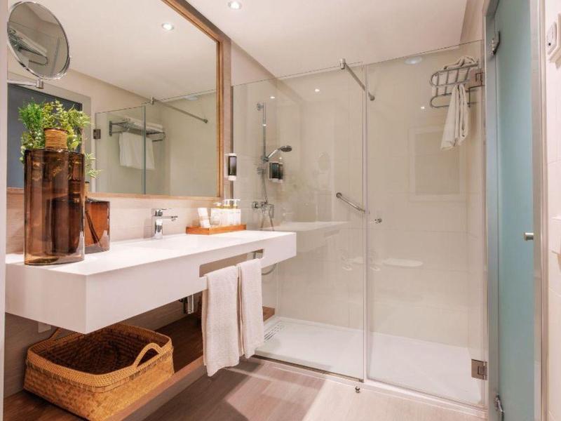 Baño claro con amplia ducha, lavabo doble y un espejo rectangular.