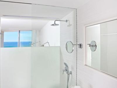 Helles, modernes Badezimmer mit großer Glasdusche, weißem Waschbecken und Meerblick durchs Fenster.