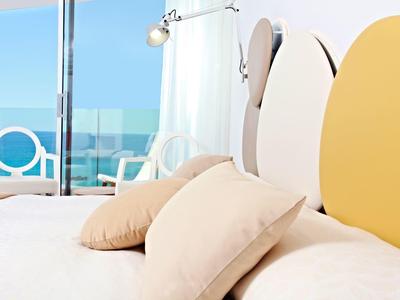 Modernes Schlafzimmer mit buntem Kopfteil, weißen Kissen und Meerblick durch Glasfenster.