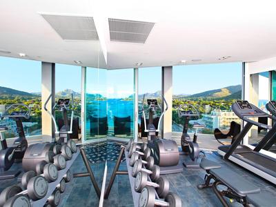 Helles Fitnessstudio mit Hanteln, Laufbändern und Panoramafenstern mit Bergblick.