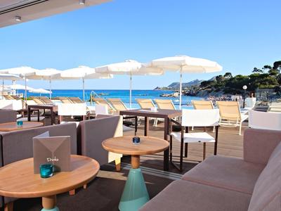 Freiluft-Café mit Holztischen, weißen Sonnenschirmen und Blick aufs blaue Meer.