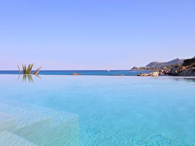 Ein klarer blauer Infinity-Pool mit Blick auf das ruhige Meer und Berge im Hintergrund.