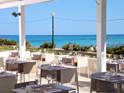 Freiluftrestaurant mit weißen Möbeln und Blick auf das blaue Meer unter klarem Himmel.