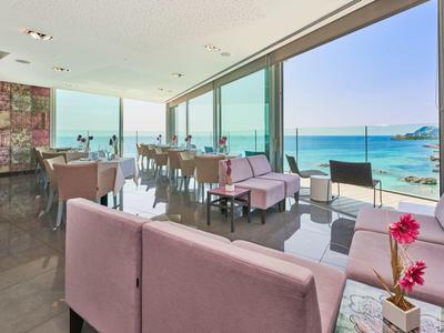 Moderner, heller Sitzbereich mit rosa Sofas, Tischen und großer Glasfront zum blauen Meer.