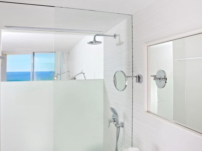 Helles, modernes Badezimmer mit großer Glasdusche, weißem Waschbecken und Meerblick durchs Fenster.