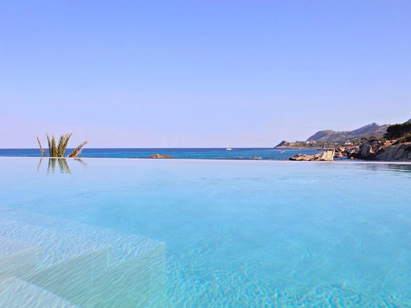 Ein klarer blauer Infinity-Pool mit Blick auf das ruhige Meer und Berge im Hintergrund.