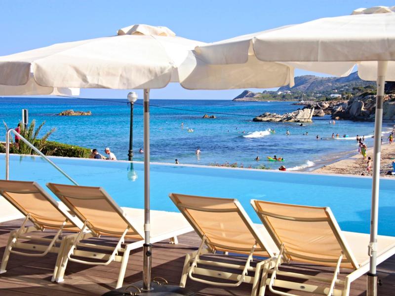 Strandliegen mit Sonnenschirmen am türkisblauen Meer unter klarem Himmel.