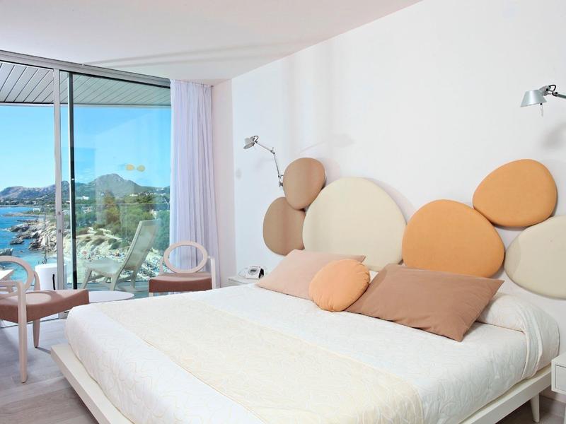 Modernes Schlafzimmer mit großem Bett und buntem Polster-Kopfteil, Panoramafenster mit Meerblick.