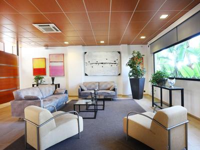 Espace lounge moderne d'hôtel avec fauteuils, canapés, grand écran et plantes.