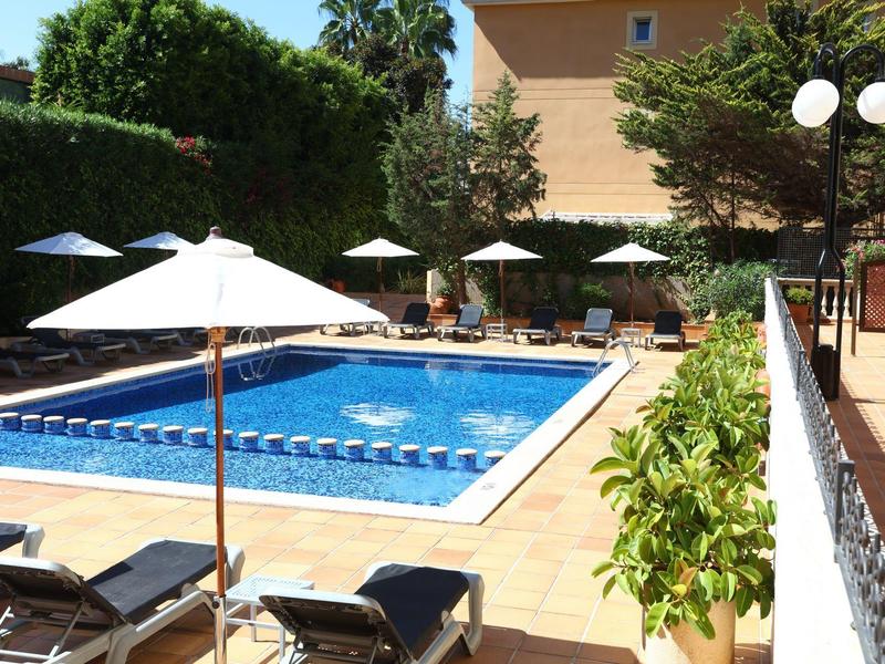 Obdélníkový bazén s modrou vodou, obklopený slunečníky a lehátky.