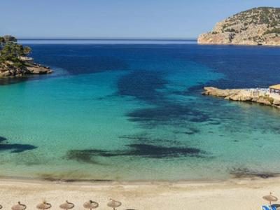 Klares, türkisblaues Meer umgeben von Felsen mit weißem Sandstrand und Sonnenschirmen.