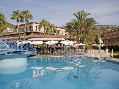 Großer Pool mit blauem Wasser, Sonnenschirmen und Palmen in Hotelanlage.