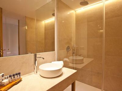 Modernes Badezimmer mit rundem Waschbecken, Wasserhahn, großer Spiegel und beige Wandfliesen.