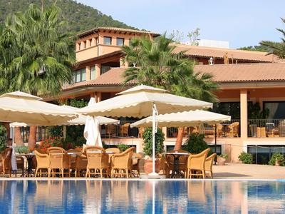 Hotelterrasse mit Sonnenschirmen und Pool vor Palmen und Gebäude.