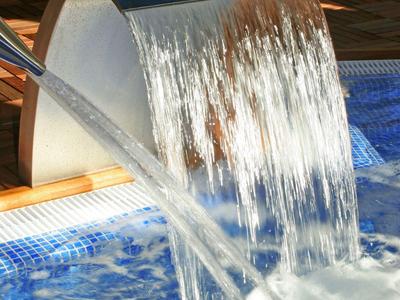 Stainless steel waterfall flows into a blue hotel pool with a hot tub in the background.