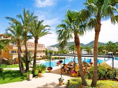 Hotelgarten mit Palmen und großer Poollandschaft bei sonnigem Wetter.