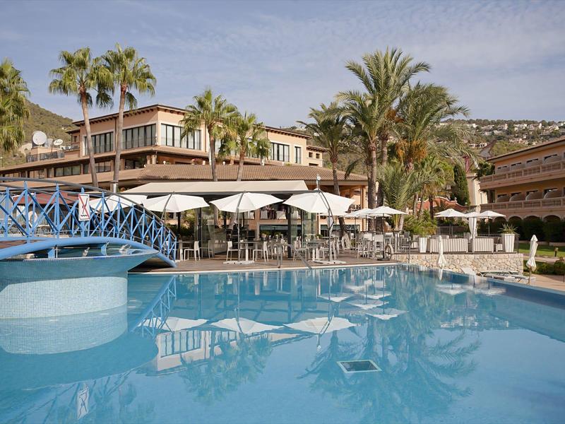 Großer Pool mit blauem Wasser, Sonnenschirmen und Palmen in Hotelanlage.