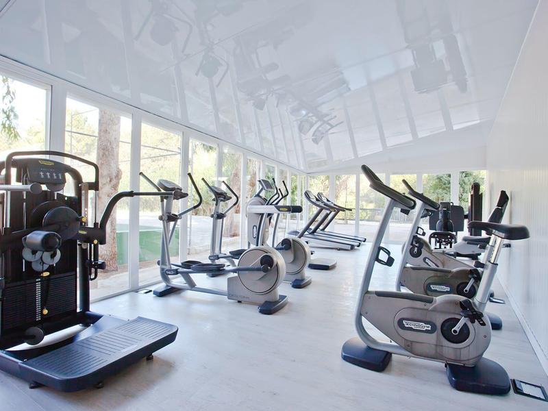 Fitnessraum mit modernen Trainingsgeräten, großen Fenstern und hellen, offenen Raum.