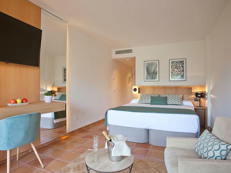 Helles Schlafzimmer mit Doppelbett, blauem Sessel, Couch, Schreibtisch und zwei Bildern an der Wand.