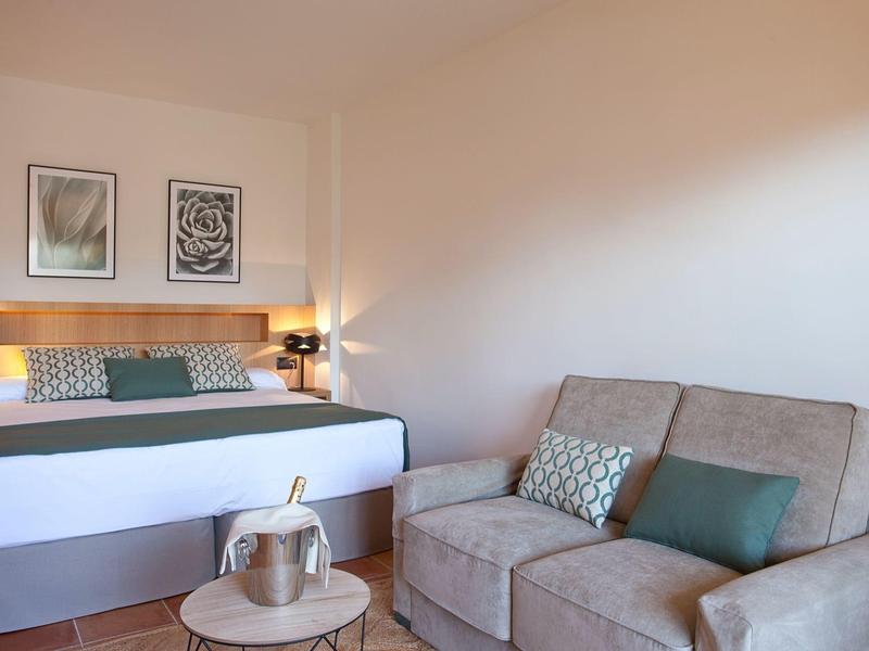 Gemütlicher Hotelraum mit Doppelbett, Sofa, Tisch und moderner Dekoration.