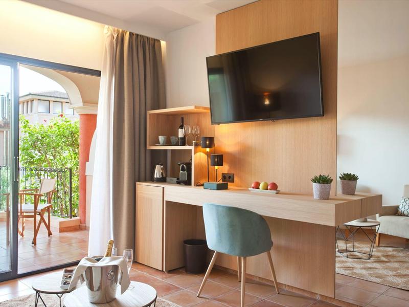 Moderner Raum mit Holzschreibtisch, Fernseher, blauem Stuhl, Glas-Schiebetür und Balkon mit Stühlen.