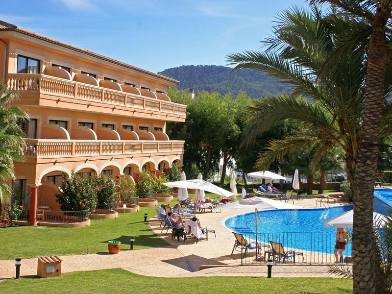 Hotel mit Außenpool, Sonnenschirmen und Liegestühlen in tropischer Gartenanlage.