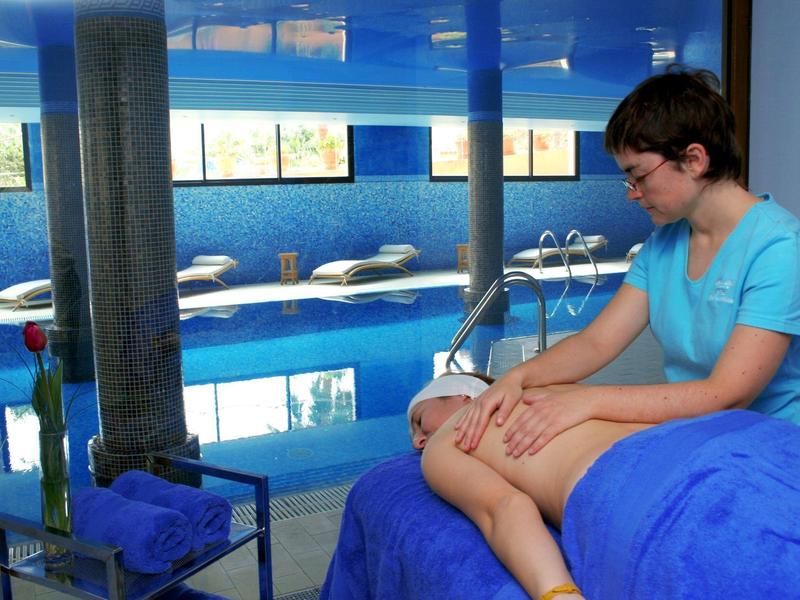 Entspannte Massagebehandlung neben einem Innenpool mit blauer Einrichtung und Tageslichtfenstern.