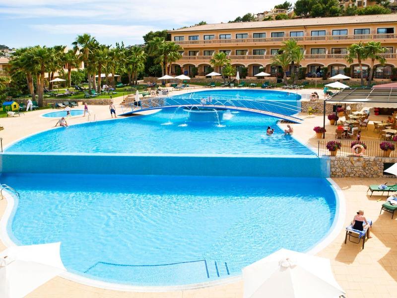 Großer Außenpool mit blauem Wasser, umgeben von Sonnenliegen und einem Hotelgebäude im Hintergrund.