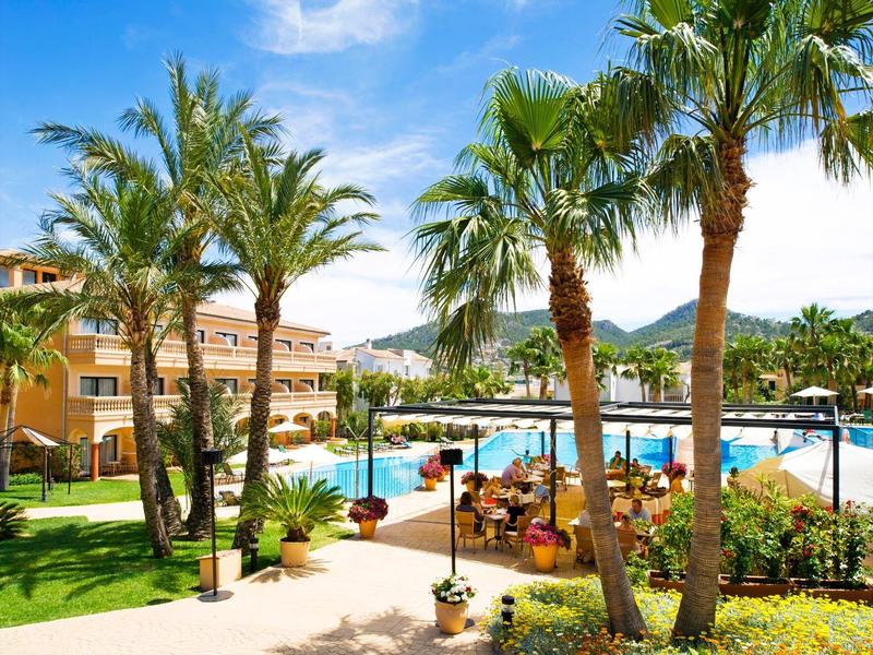 Hotelgarten mit Palmen und großer Poollandschaft bei sonnigem Wetter.