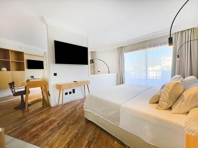 Habitación de hotel moderna con cama doble, ventana grande, suelo de madera y pantalla de TV.