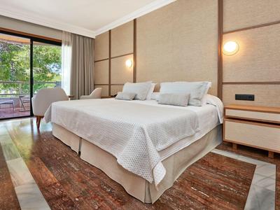 Habitación de hotel moderna con dos camas, mesitas de noche y vista a una terraza con árboles.