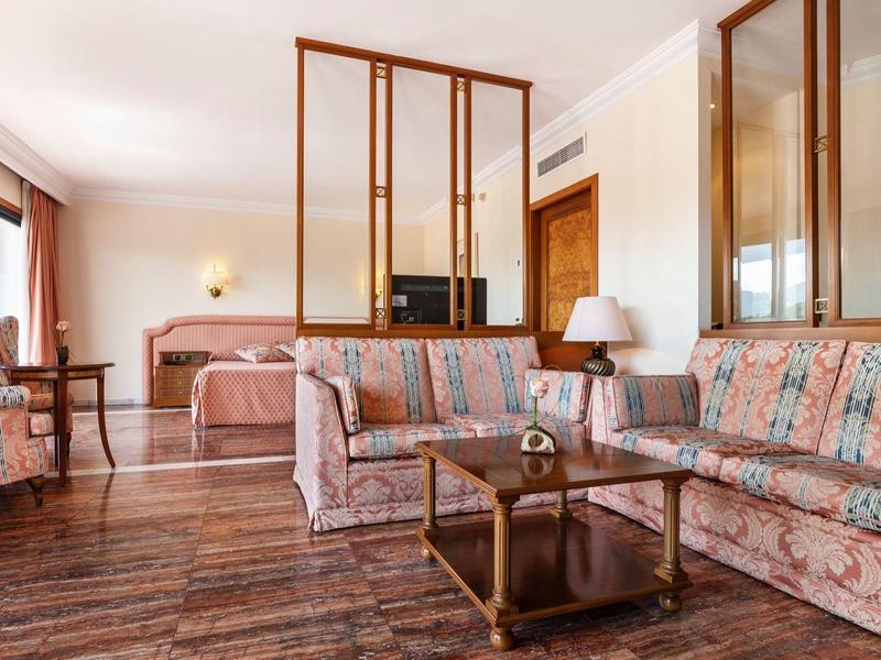 Sala acogedora con sofá floral, sillón y suelo de madera en una habitación de hotel.