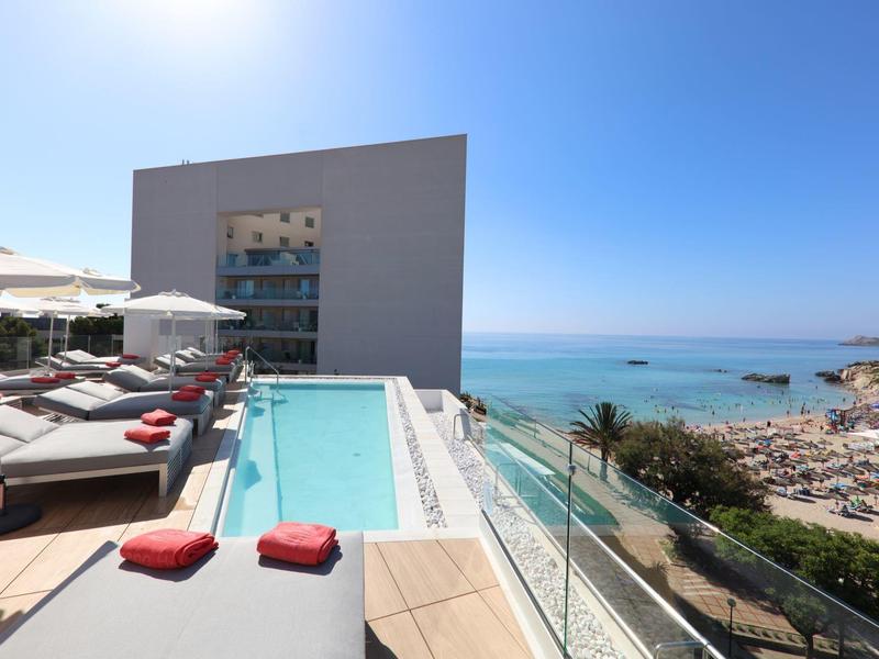 Piscina infinita en una terraza con vista al mar y una playa bajo un clima soleado.