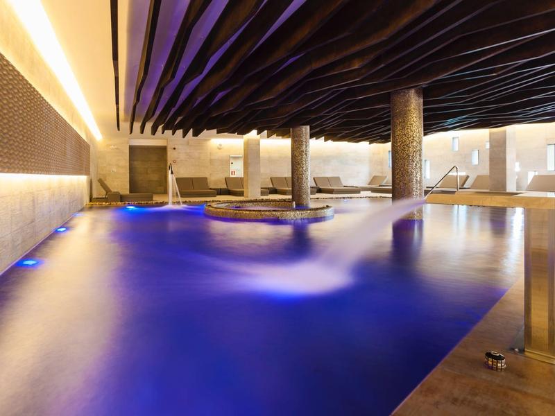 Piscina interior con iluminación azul, columnas y techos modernos en un área de hotel