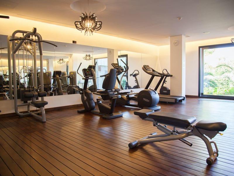 Gimnasio moderno con suelo de madera, máquinas de cardio y fuerza, espejos grandes y luz natural.