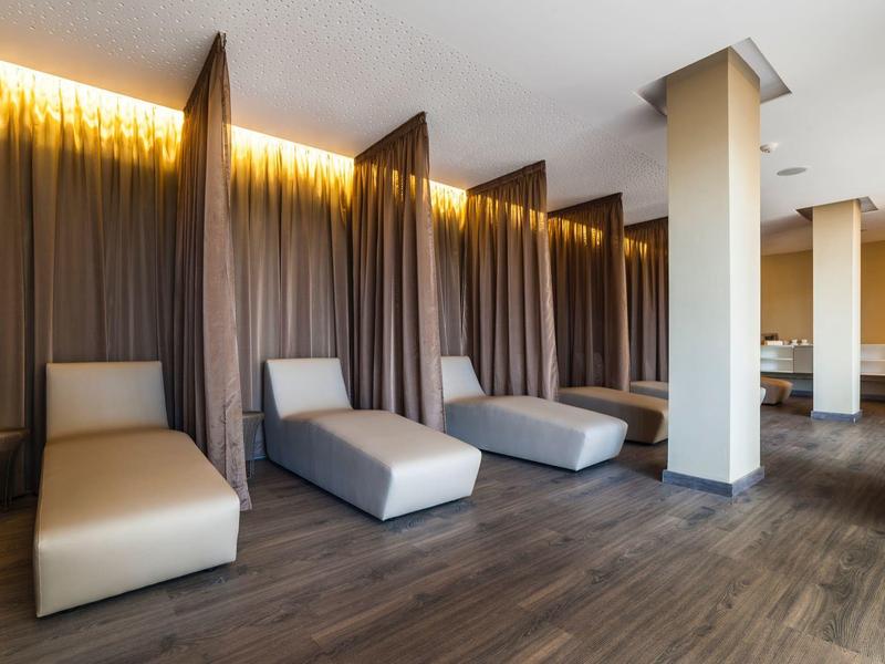 Sala de descanso moderna con tumbonas, luz indirecta y suelo de madera oscura en un hotel.