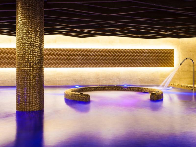 Piscina interior moderna con luz cálida, columna redonda y ambiente relajante en el hotel.