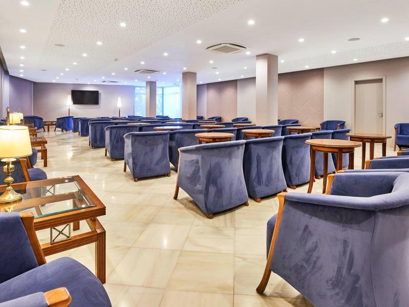 Sala de conferencias con sillas tapizadas azules y mesas de madera, iluminada y con diseño moderno.