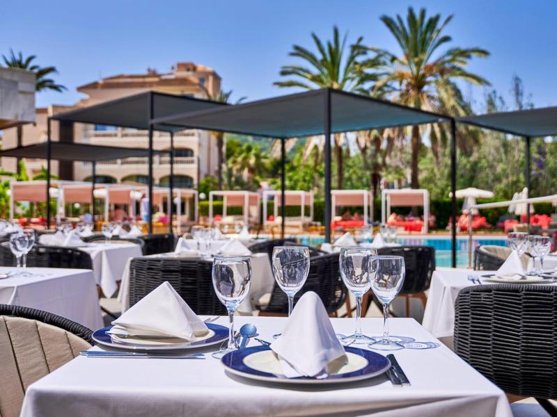 Mesa elegante al aire libre en hotel con mantel blanco, copas y servilletas bajo sol.