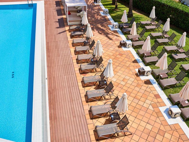 Vista aérea de una piscina de hotel con sombrillas y tumbonas alineadas ordenadamente.