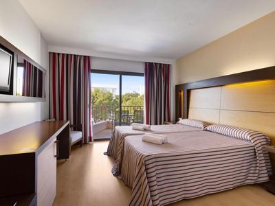 Brightly furnished hotel room with double bed and terrace overlooking green trees.