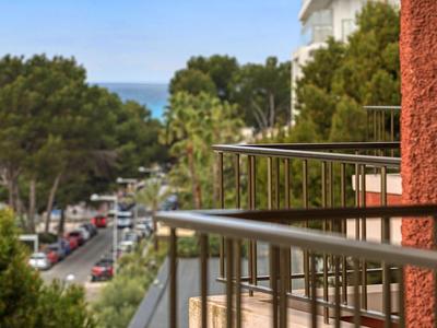 View from a balcony with metal railing onto a tree-lined street and the sea in the background.
