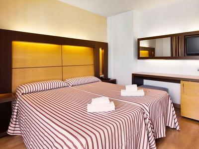 Modern hotel room with double bed, striped bedspread, and wall mirrors beside a TV.