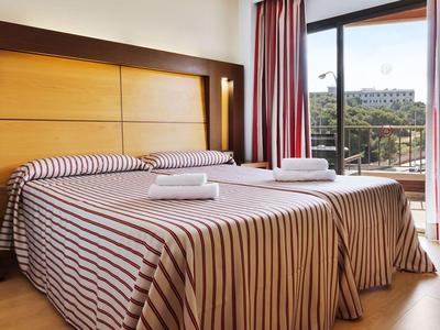 Hotelkamer met twee eenpersoonsbedden, gestreept beddengoed en een balkon met uitzicht op de stad.