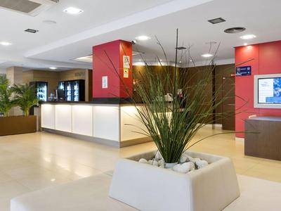 Hotel reception with illuminated counter, seating area, and plant in the foreground.