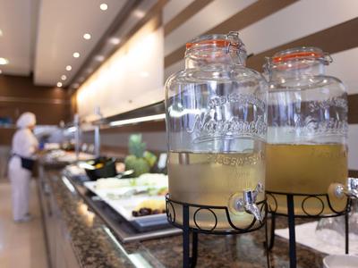 Two beverage dispensers with juice on a hotel buffet counter, staff in the background.