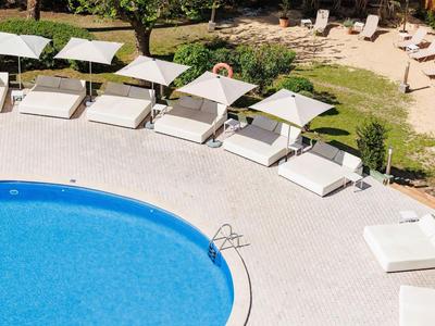 Blue pool with multiple white sun loungers and umbrellas on a gray surface under sunny weather.